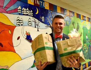 man holding two bags of groceries in a elementary school hallway with paintings on the walls