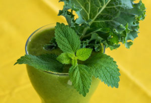 green smoothie in glass with mint and kale leaves on top