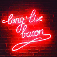 a neon sign on a brick wall that glows with Long Live Bacon