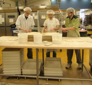 three bakers standing at a table with pieces of dough spread in front of them