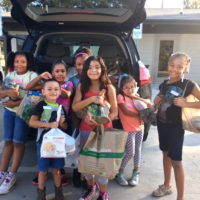 7 children holding bags of produce by a car