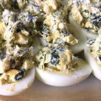 a plate of deviled eggs, they have green spinach in the yolks