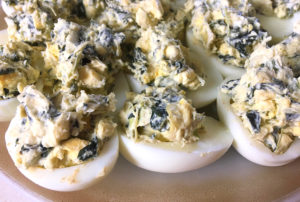 a plate of deviled eggs, they have green spinach in the yolks
