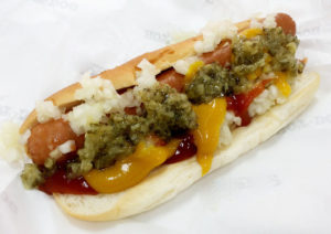 a hot dog in a bun with relish, chopped onion, mustard, and ketchup