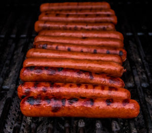 a row of hot dogs roasting on a grill