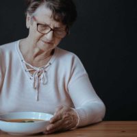older woman sitting at table looking at bowl of soup