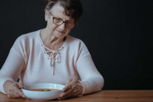 older woman sitting at table looking at bowl of soup