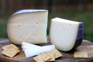 two rounded wedges of cheese with holes and dark rind, with crackers on board
