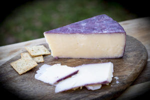 wedge of cheese with red-wine-colored rind on board with some slices and crackers