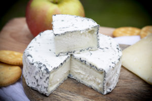 a wheel of cheese with one wedge cut out and resting on top; it has a thick rind that's a different color, like blue cheese