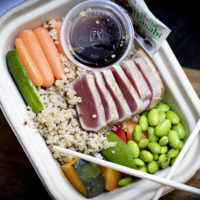 tray with quinoa, soybeans, raw vegetables, soy sauce in containers, wasabi packet, and slices of raw tuna, with chopsticks crossed on top