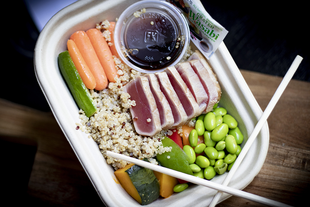 tray with quinoa, soybeans, raw vegetables, soy sauce in containers, wasabi packet, and slices of raw tuna, with chopsticks crossed on top