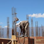 men working atop brick wall with rebar sticking up