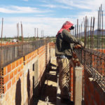 men working atop brick wall with rebar sticking up