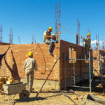 men working atop brick wall with rebar sticking up