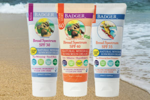 three tubes of sunscreen on a sandy beach