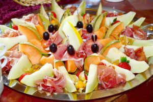 tray with slices of melon, folded pieces of fancy ham, and olives, arranged symmetrically