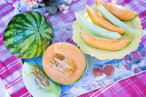 watermelon, cantaloupe, and honeydew pieces and whole on a table with flowers (top view)