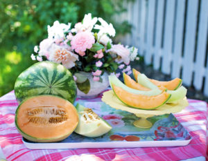 watermelon, cantaloupe, and honeydew pieces and whole on a table with flowers