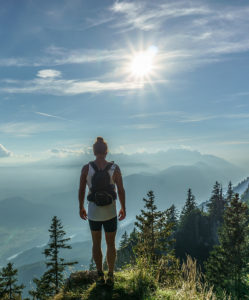 person hiking with trees and mountains with sun in sky