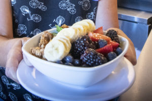 bowl with bananas, berries, and granola, held by hands