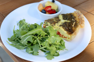 slice of quiche, salad greens, and tiny cup of fruit on plate