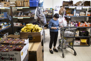 person with shopping cart checking list in aisles of food at food pantry