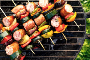 Grilled skewers of meat, sausages and various vegetables on a grill plate, outdoors, top view