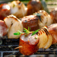 Grilled skewers with sausages and onions on a grill plate, outdoors