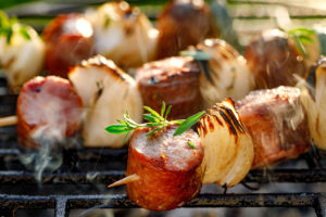 Grilled skewers with sausages and onions on a grill plate, outdoors