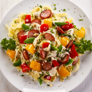 Pasta with sausages and vegetables on plate, top view