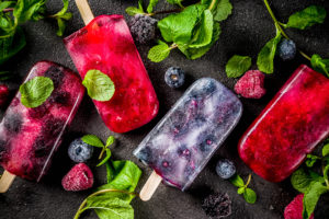 frozen pops containing clear juice and berries on a background with mint leaves and berries