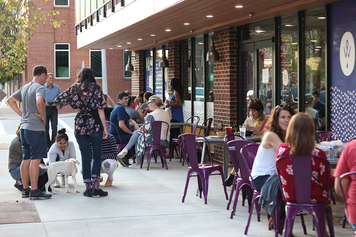 people eating at tables and petting a dog ion the sidewalk in front of Weaver Street Raleigh location