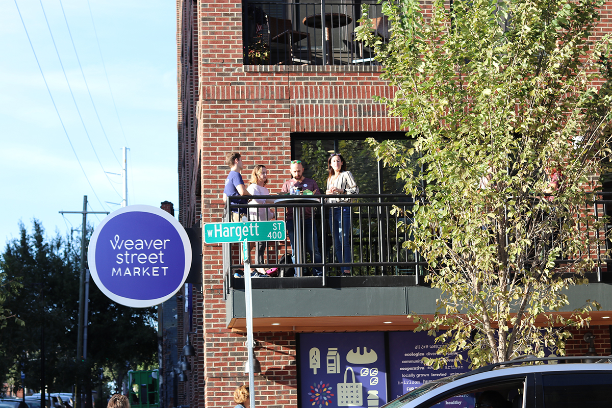 people on outdoor balcony, with Hargett St sign and Weaver Street logo sign, at Weaver Street Raleigh