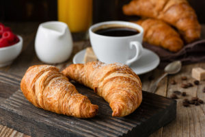 two croissants on table with cup of coffee, bowl of raspberries, spoon