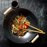 Chinese wok. Asian cellophane noodles with vegetables and chicken in a frying pan wok. On dark rustic background