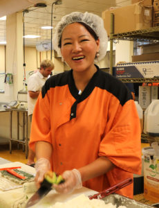 Sujin in a kitchen chef shirt, smiling and holding a knife and avocado
