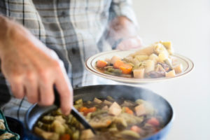 Man serving a portion of steamy, freshly homemade beef and vegetable stew.